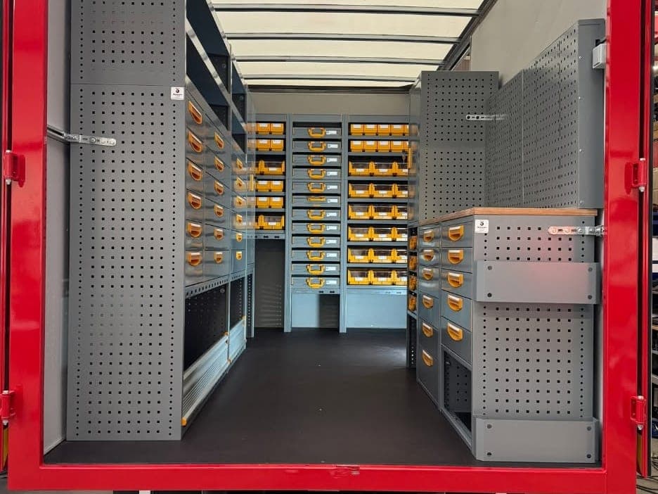 Camion atelier de Bodarwé Entreprises vu de l'arrière, portes ouvertes sur une allée bordée de rayonnages et de tiroirs Store Van