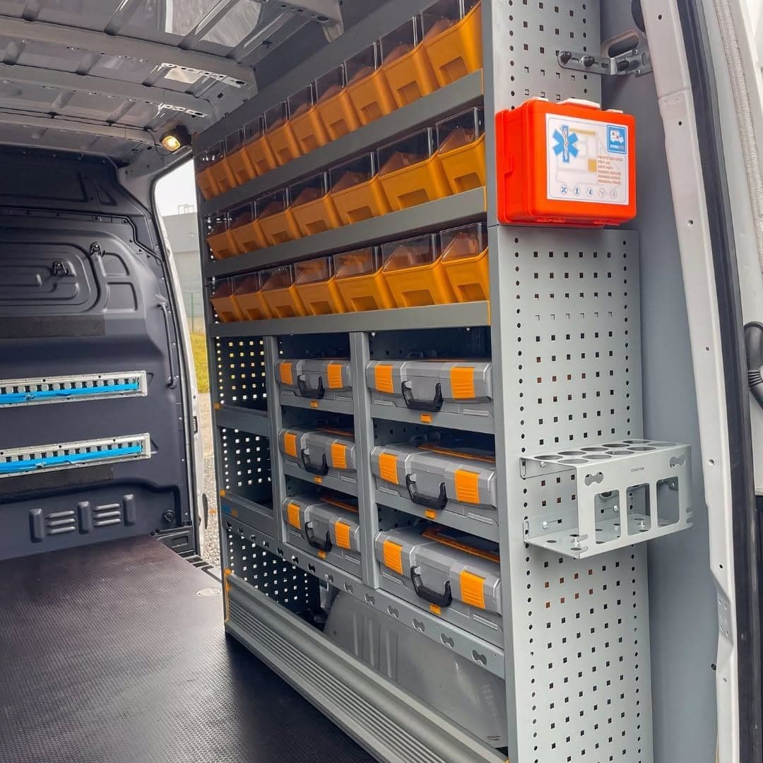 Côté droit de la zone de chargement de Bovy Chauffage, bacs orange transparents, coffrets empilés, trousse de premiers secours et support de cartouches