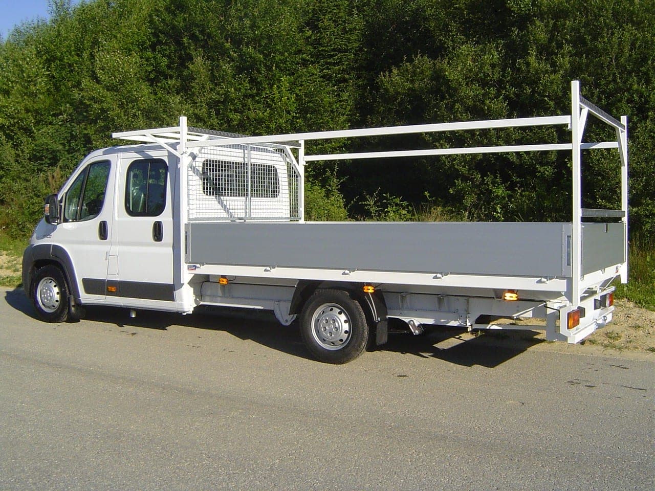 Plateau à ridelles aluminium avec arceau porte-échelle et cloison grillagée sur un Fiat Ducato blanc