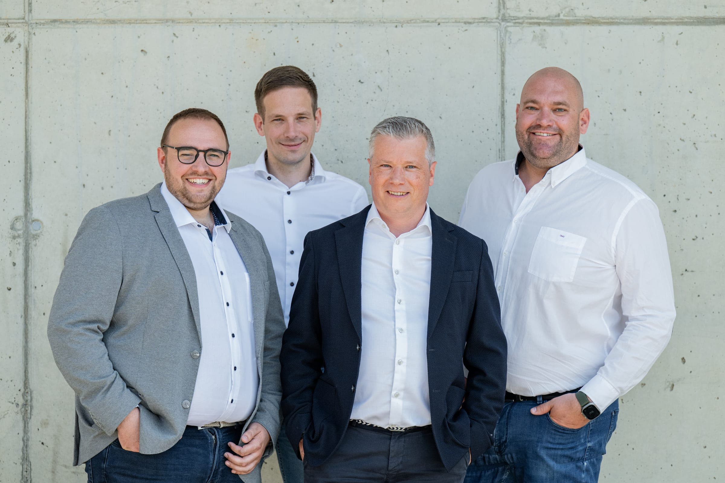 Portrait de groupe de quatre collaborateurs du bureau d’Amecam Van Conversion devant les ateliers de Francorchamps