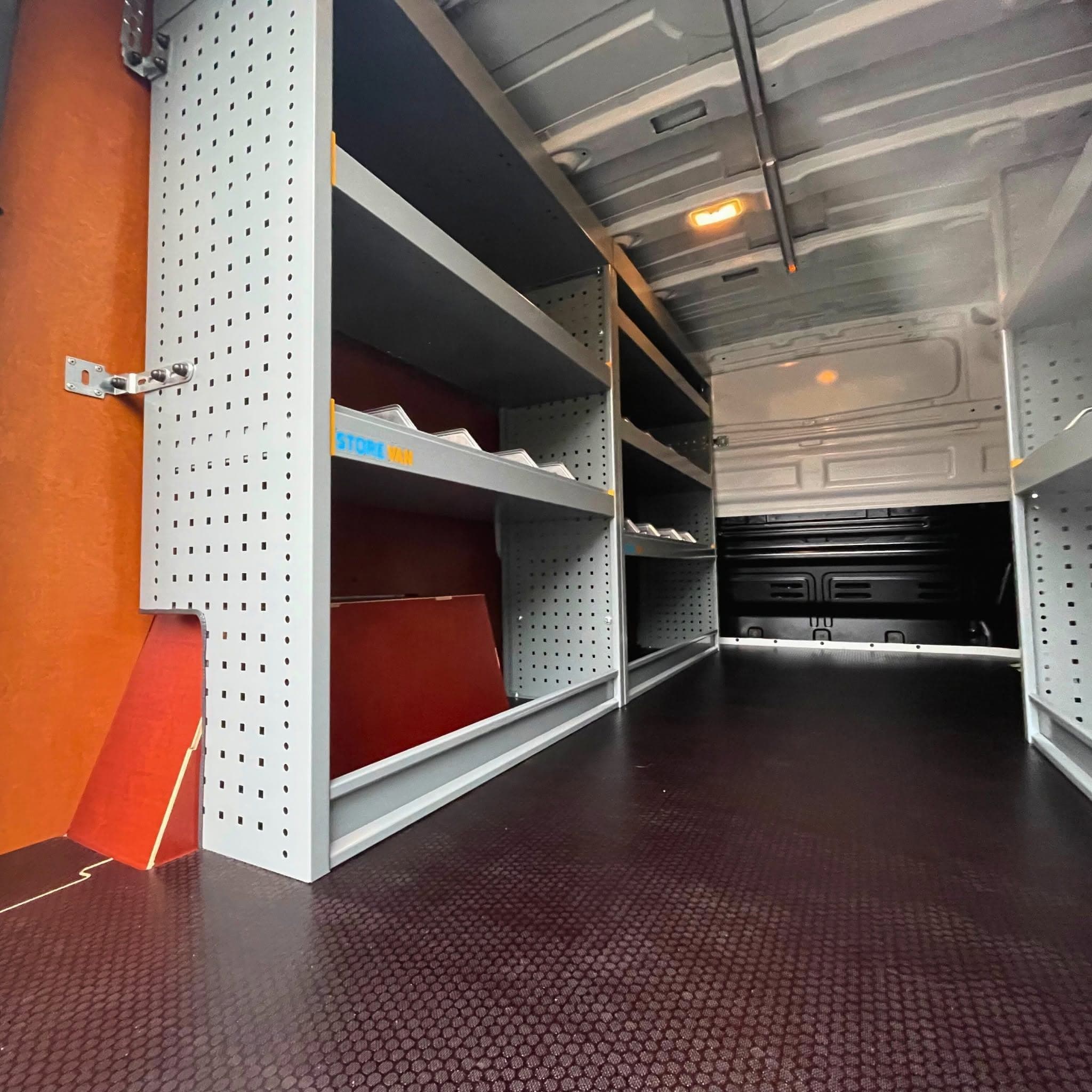 Rayonnage Store Van en tôle perforée grise contre une paroi habillée de bois, plancher antidérapant noir et éclairage de plafond