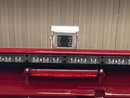 Caméra de recul fixée en haut du cadre arrière rouge, au-dessus d'une rampe de feux à LED