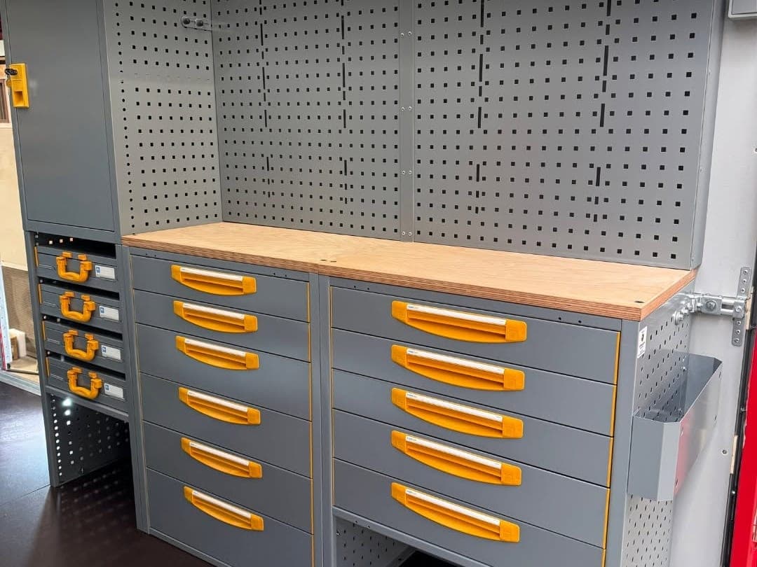 Plan de travail en bois posé sur deux blocs de tiroirs, avec panneau perforé pour l'outillage et armoire haute à côté