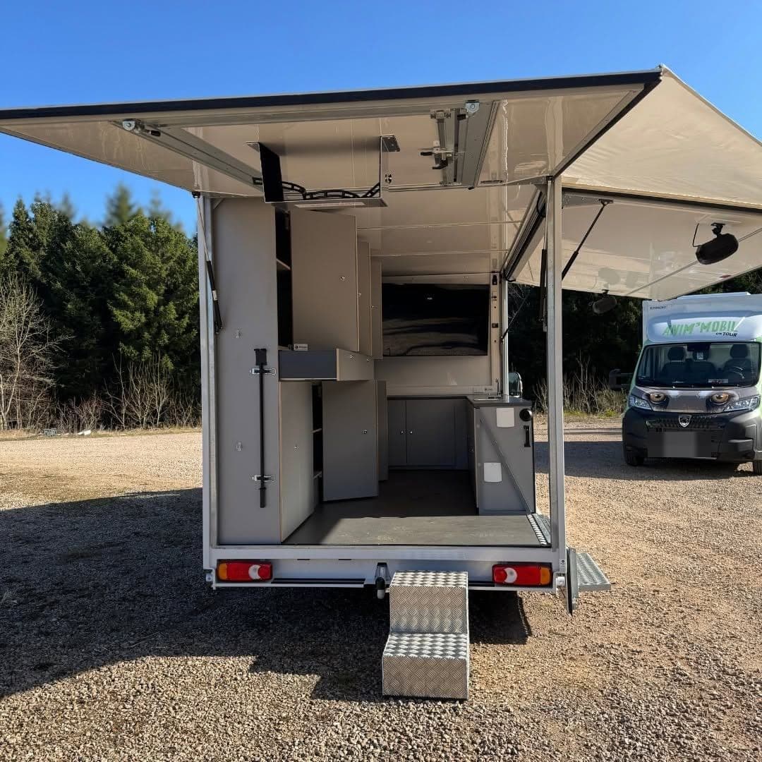 Camion Anim'mobil vu de l'arrière, côtés relevés sur les armoires et le comptoir, marche d'accès en aluminium larmé