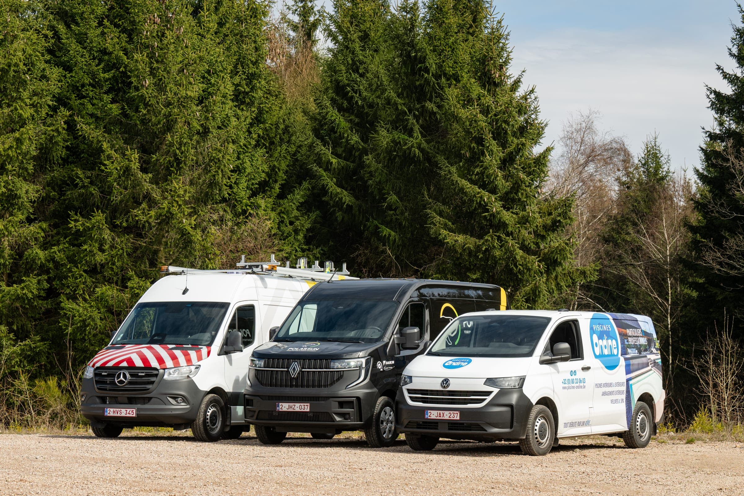 Trois utilitaires aménagés par Amecam alignés devant la sapinière : Sprinter de signalisation, Master et Transporter lettrés