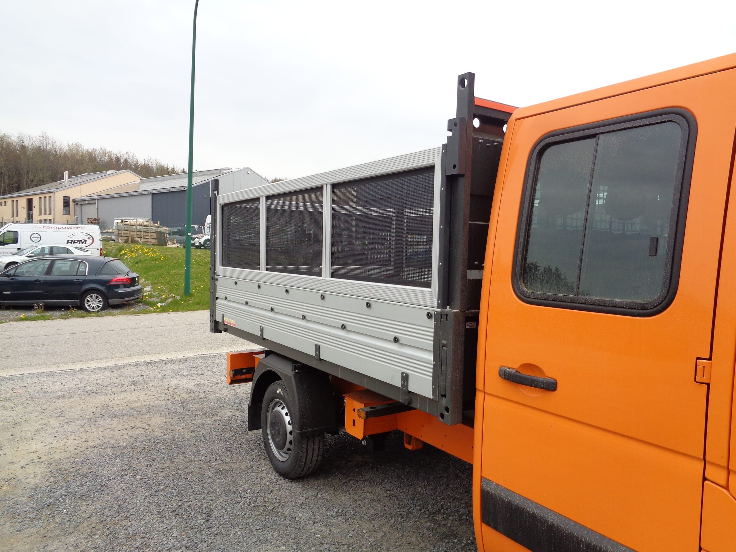 Benne à ridelles rehaussées et parois grillagées installée sur un châssis-cabine orange