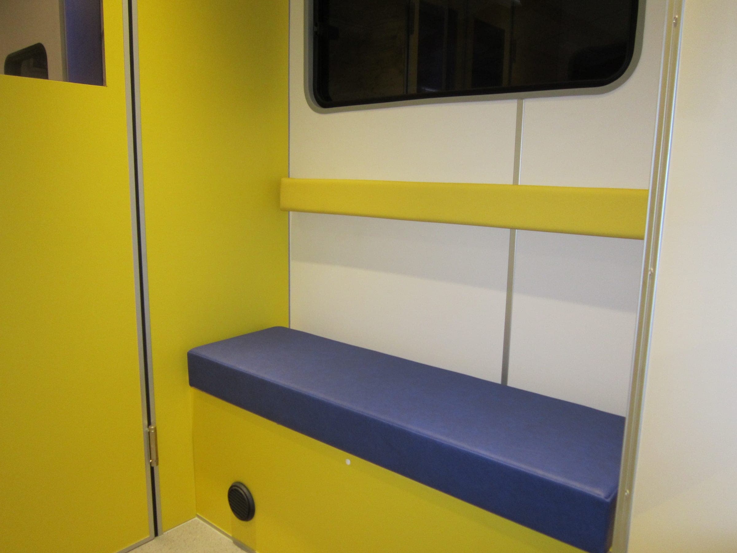 Banquette violette installée le long d’une paroi jaune et blanche dans une unité mobile, avec hublot vitré