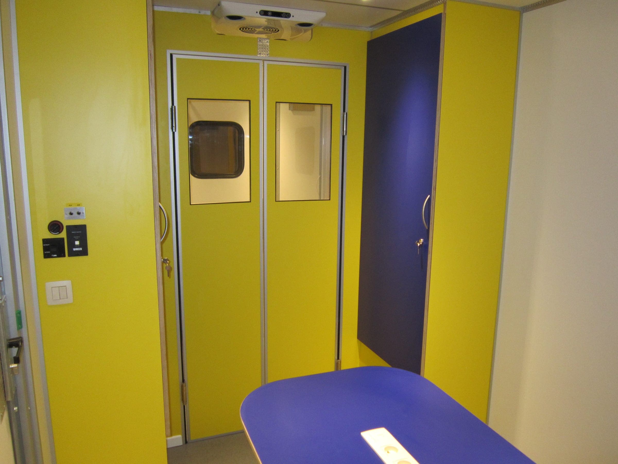 Cabine d’une unité mobile aux parois jaunes et violettes, double porte vitrée et table d’examen