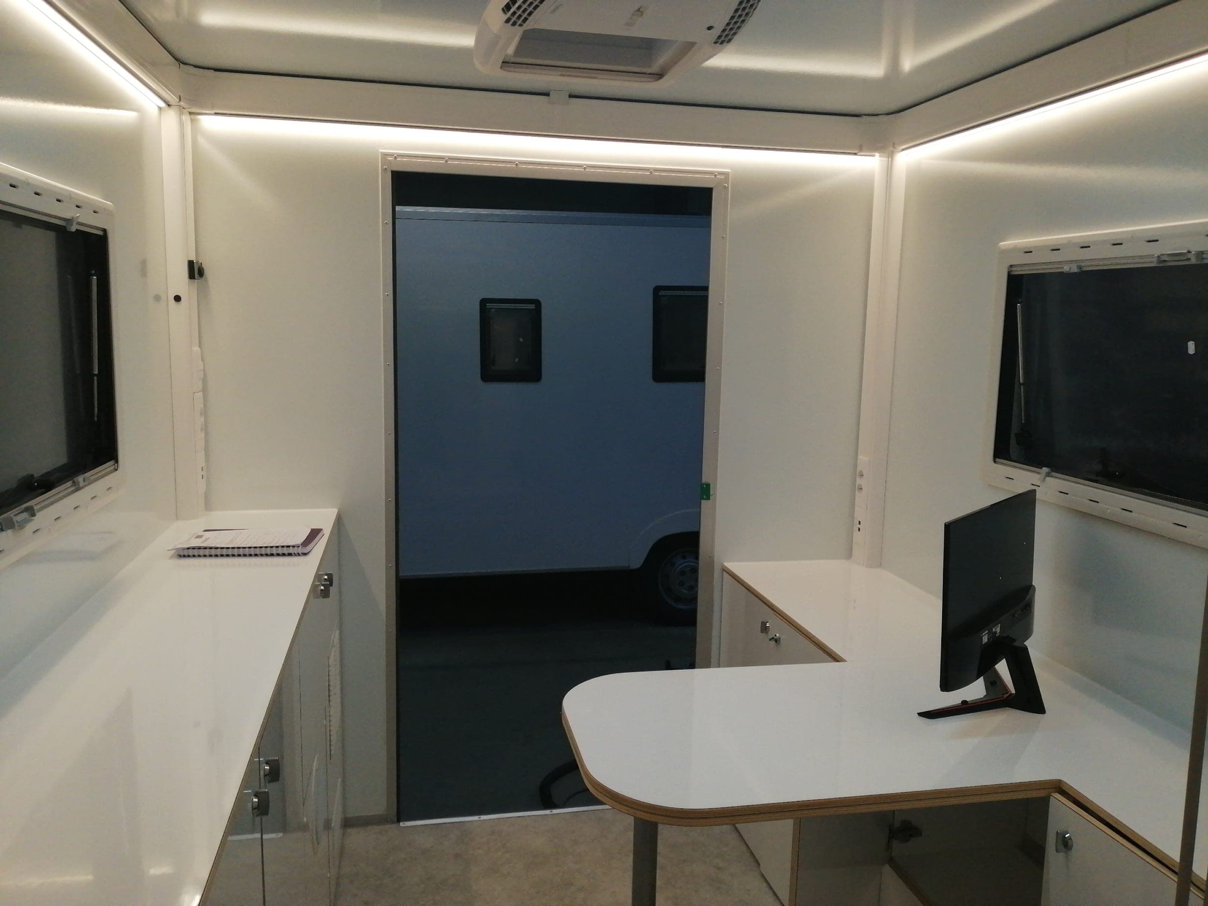 Bureau mobile équipé de deux postes de travail à plans blancs en angle, sous un éclairage indirect de plafond