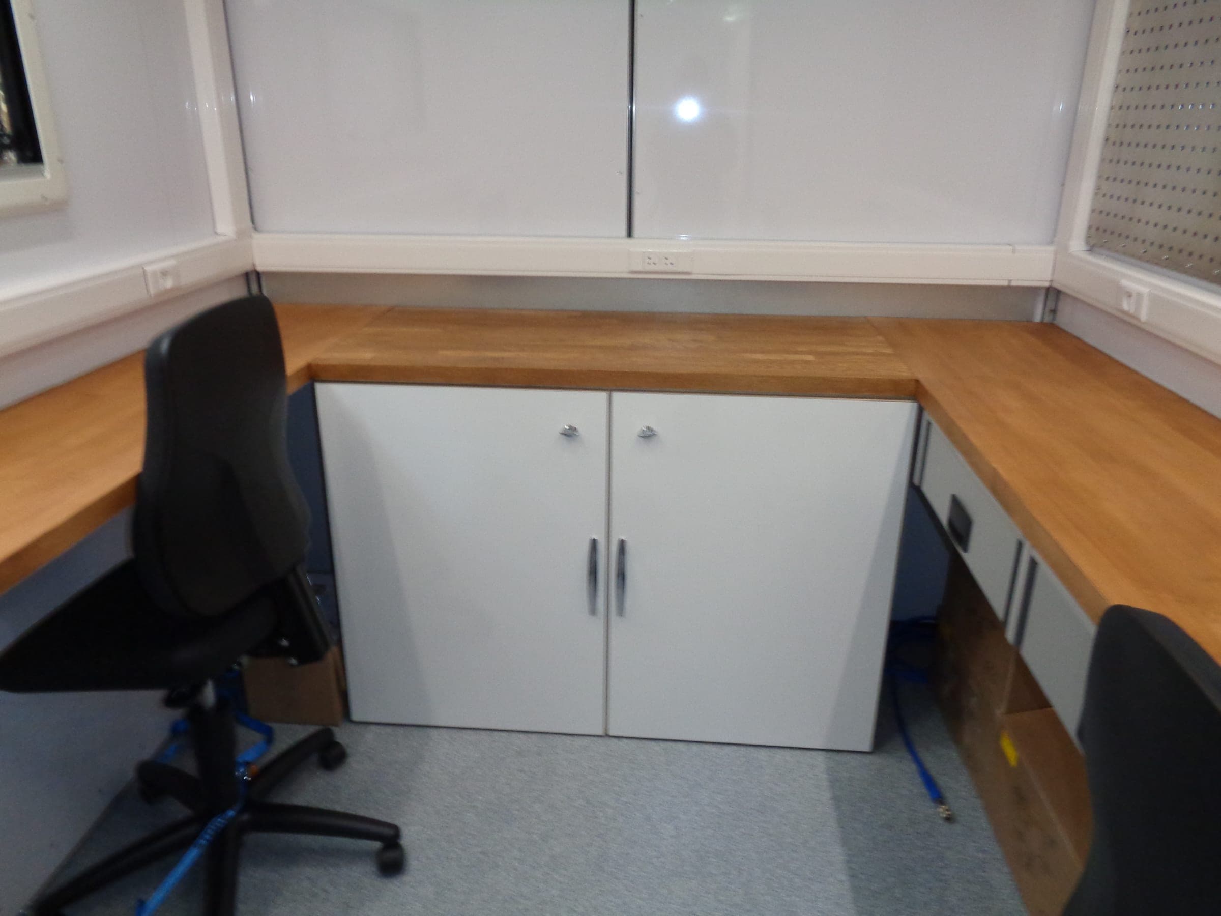 Bureau mobile avec plan de travail en bois formant un angle, siège à roulettes et placards blancs