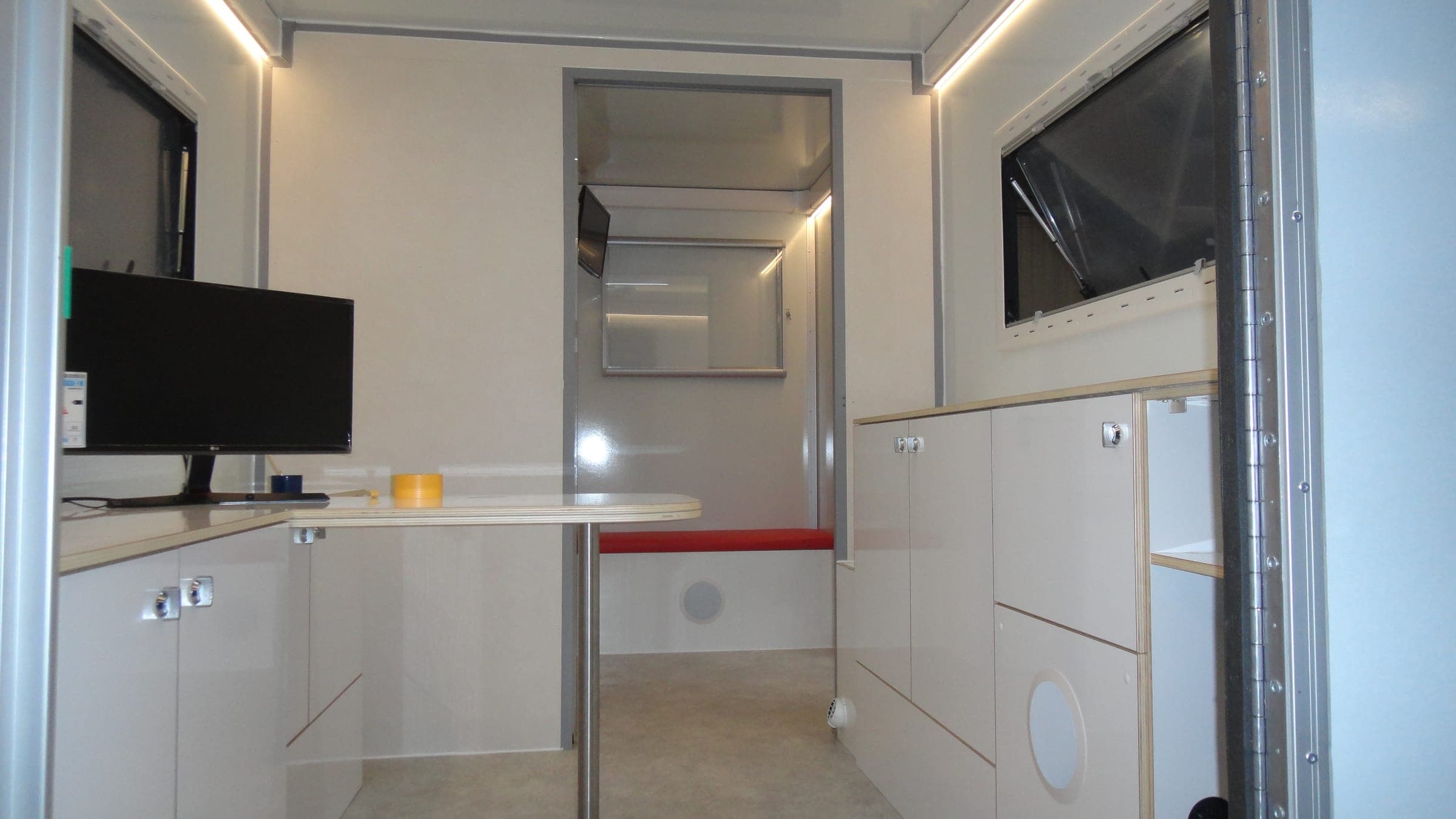 Intérieur d’un bureau mobile : poste informatique, plan de travail blanc et rangements bas et hauts