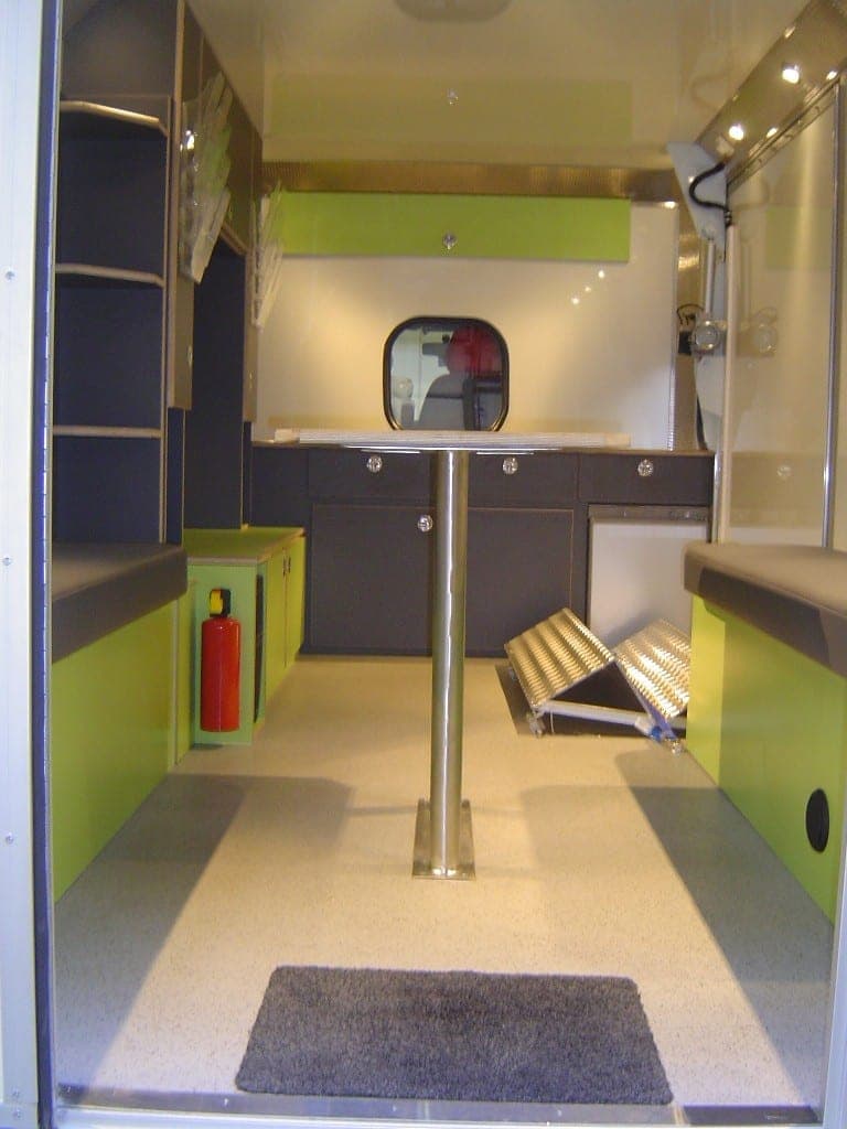 Espace d’accueil d’un bureau mobile, table haute centrale, hublot, meubles bas anthracite et rampe d’accès repliée