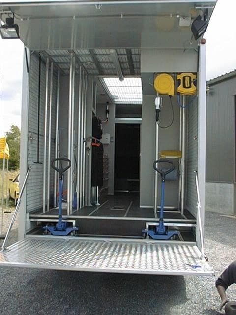 Arrière d’un camion atelier, hayon abaissé, deux transpalettes, enrouleurs jaunes et parois grillagées
