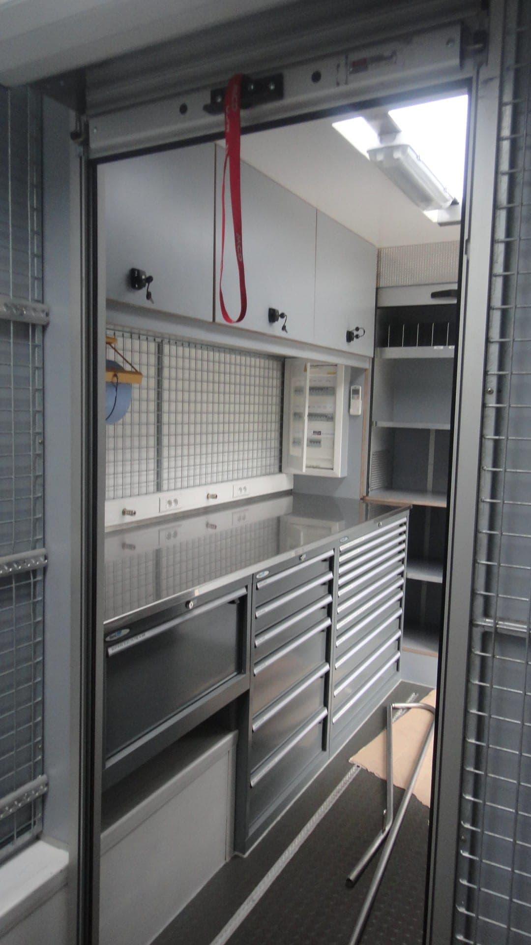 Intérieur d’un camion atelier de compétition : bloc de tiroirs inox sous un plan de travail, tabouret rangé à côté