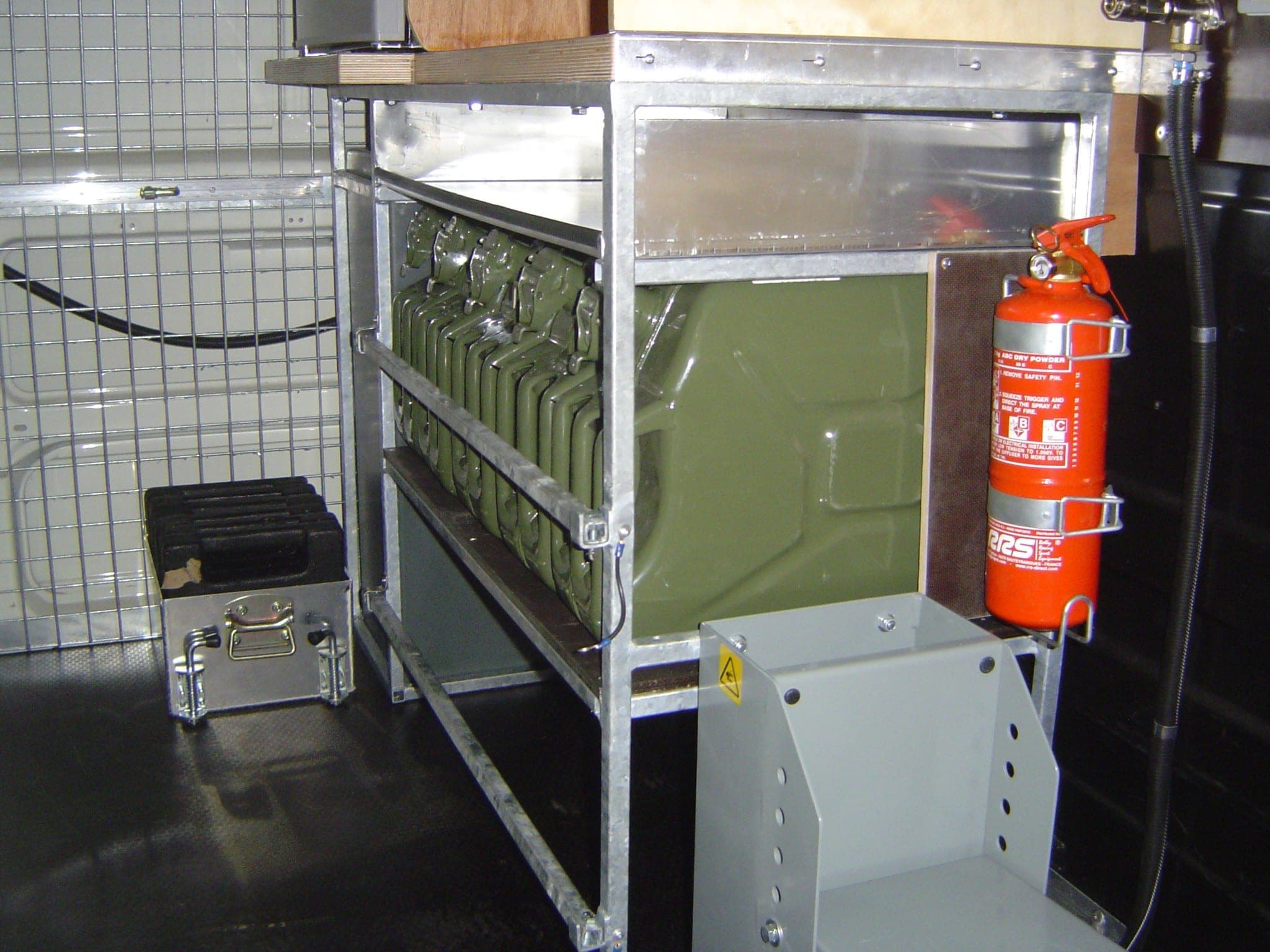 Rack de bidons sur structure galvanisée avec extincteur, installé dans un compartiment grillagé de véhicule d’assistance
