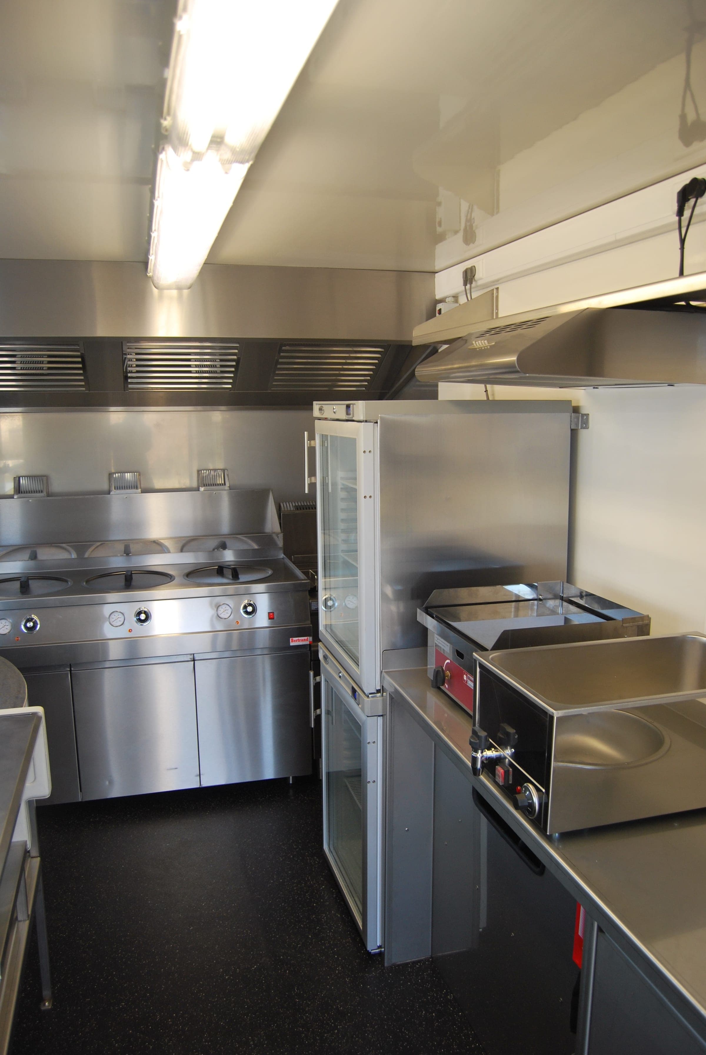 Cuisine de food truck équipée de bacs chauffants, d’une plancha et d’armoires réfrigérées vitrées