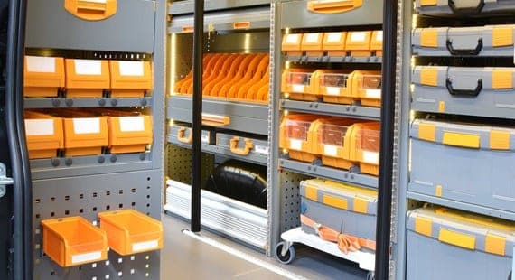 Intérieur d’un fourgon équipé, bacs à bec orange, coffrets de rangement empilés et panneau perforé sur la porte
