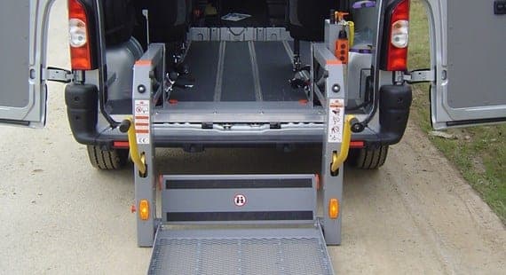 Hayon élévateur déployé à l’arrière d’un utilitaire adapté, plateforme abaissée au sol, plancher plat et rails d’ancrage visibles