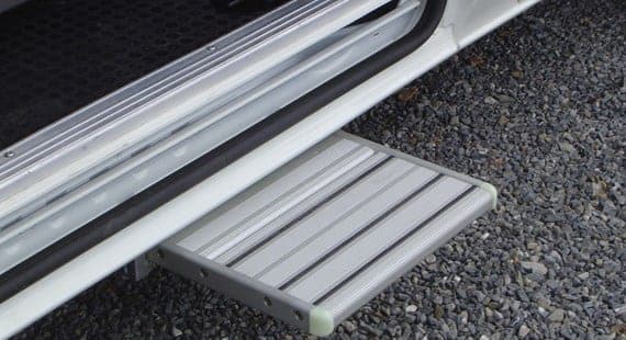 Marchepied en aluminium déployé sous la porte latérale d’un utilitaire, sur un sol en gravier