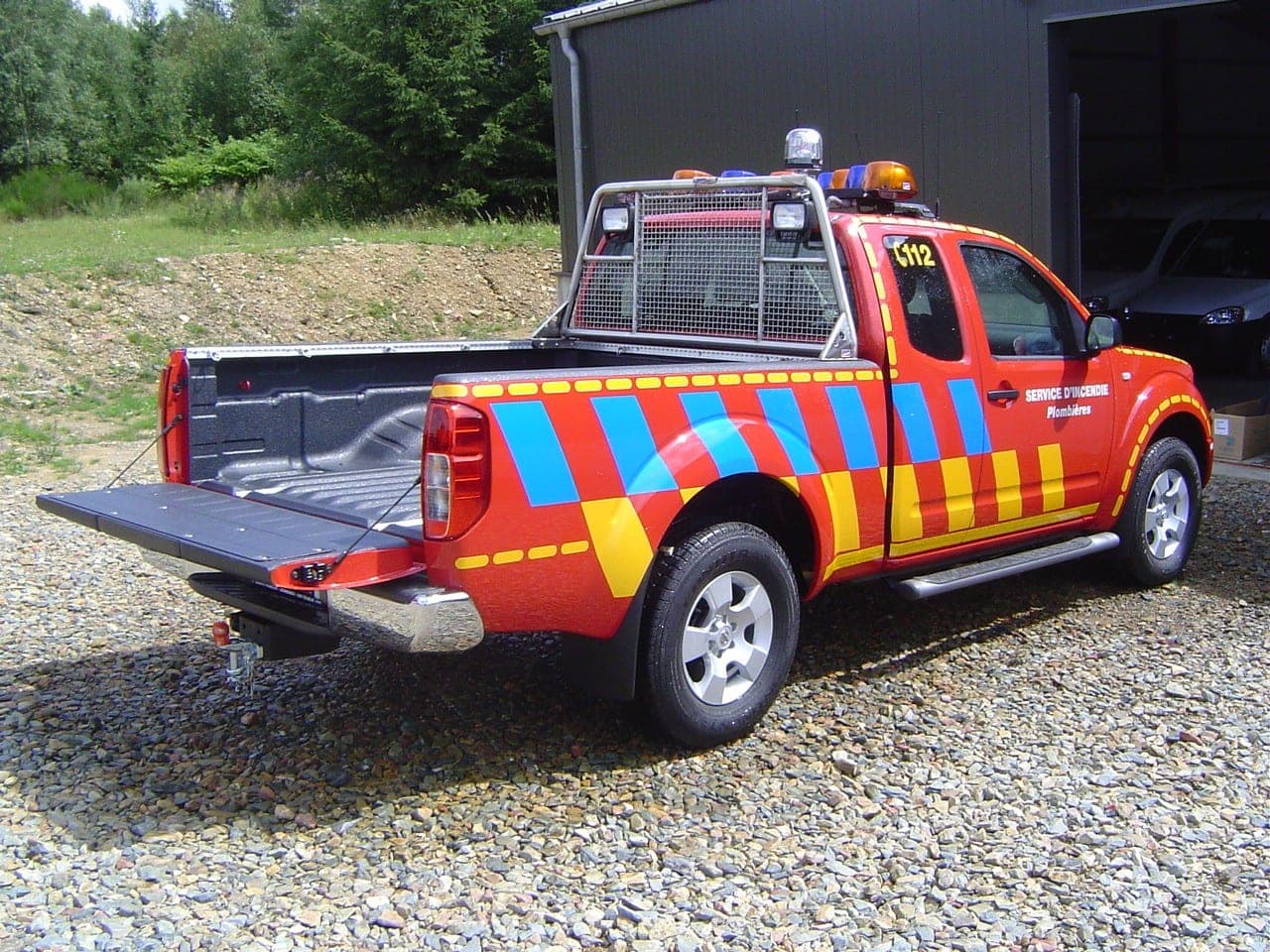 Pick-up rouge de service d’incendie, benne ouverte et arceau à gyrophares, en livrée rétroréfléchissante