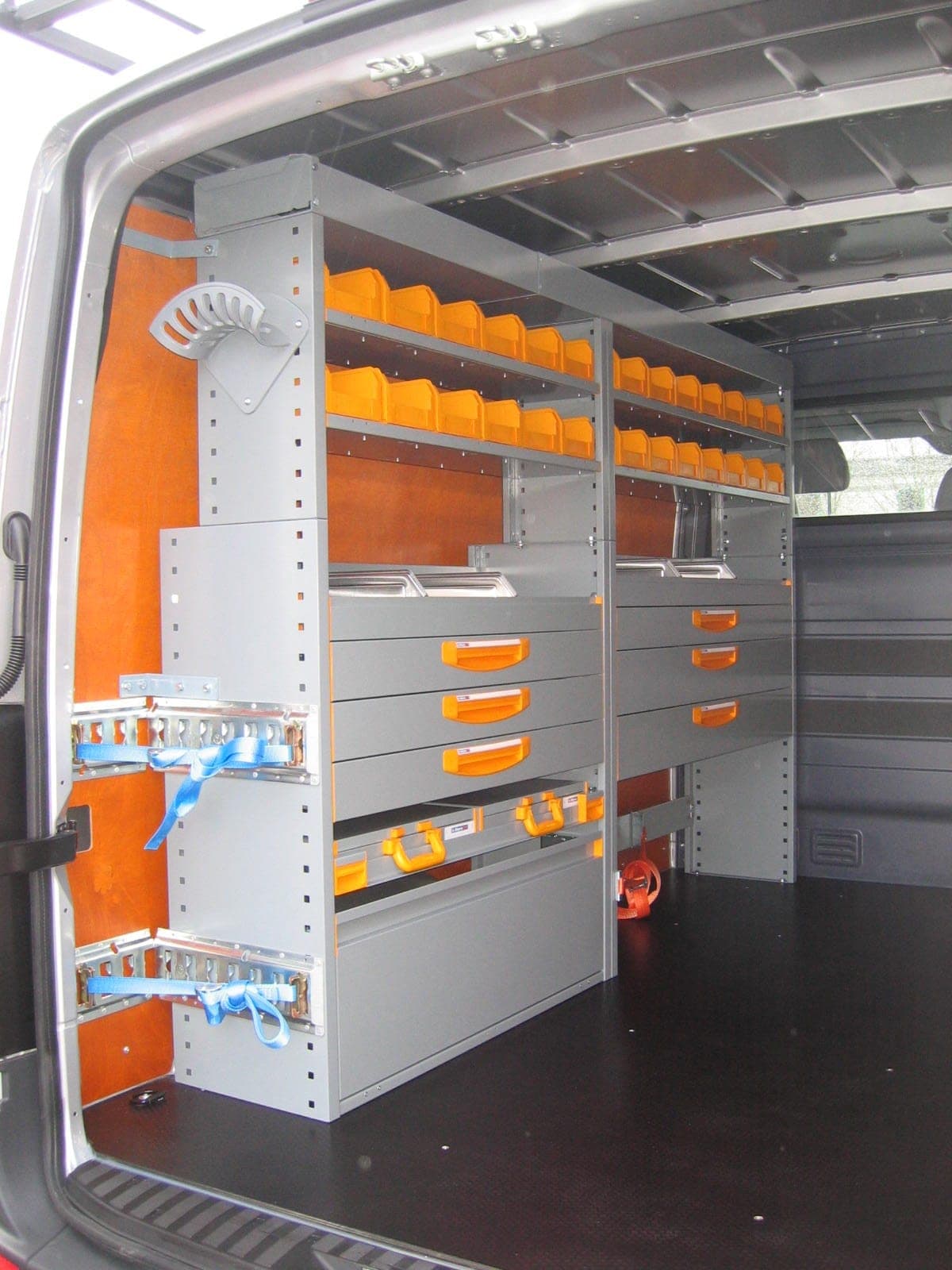 Fourgon portes arrière ouvertes sur un rayonnage aluminium à bacs orange, portes garnies de panneaux en contreplaqué
