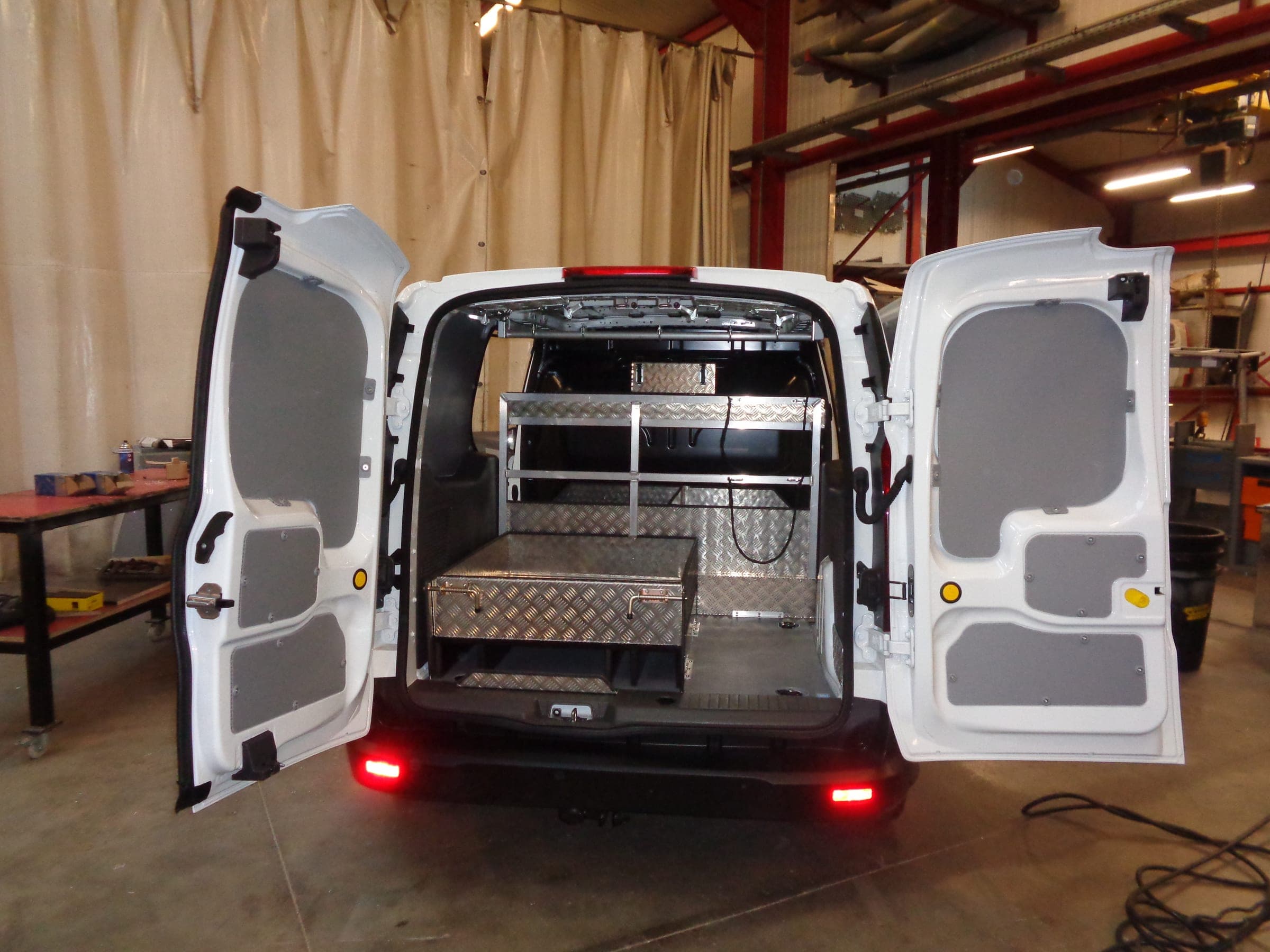 Fourgon compact portes ouvertes dans l’atelier, coffre en tôle larmée et structure aluminium à étagères