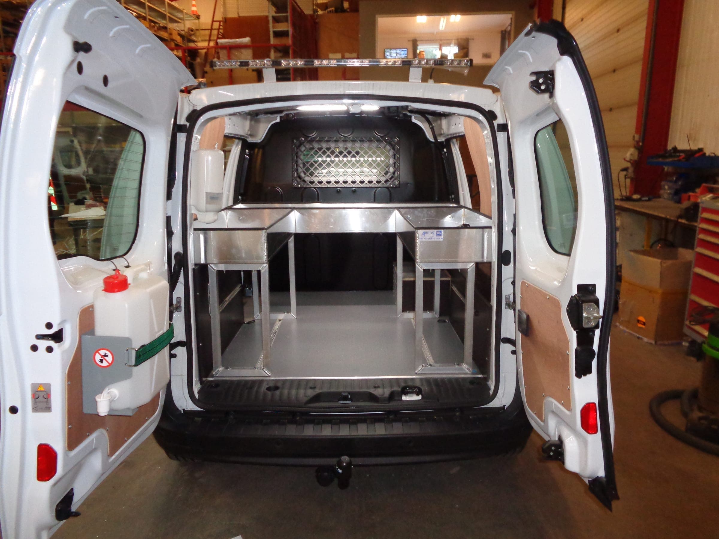 Fourgon compact portes ouvertes : structure aluminium à étagères, réservoir de lave-mains et cloison grillagée