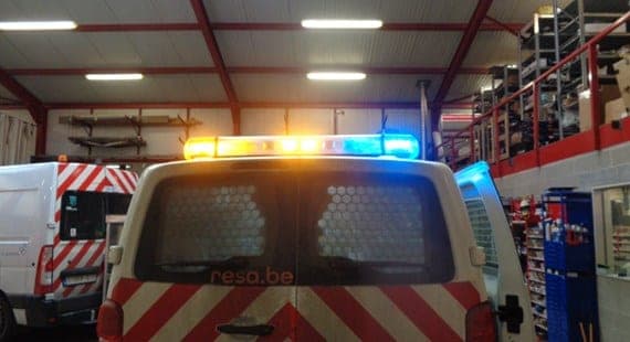 Arrière d’un utilitaire d’intervention dans l’atelier, rampe lumineuse ambre et bleue allumée, grille alvéolée sur la vitre