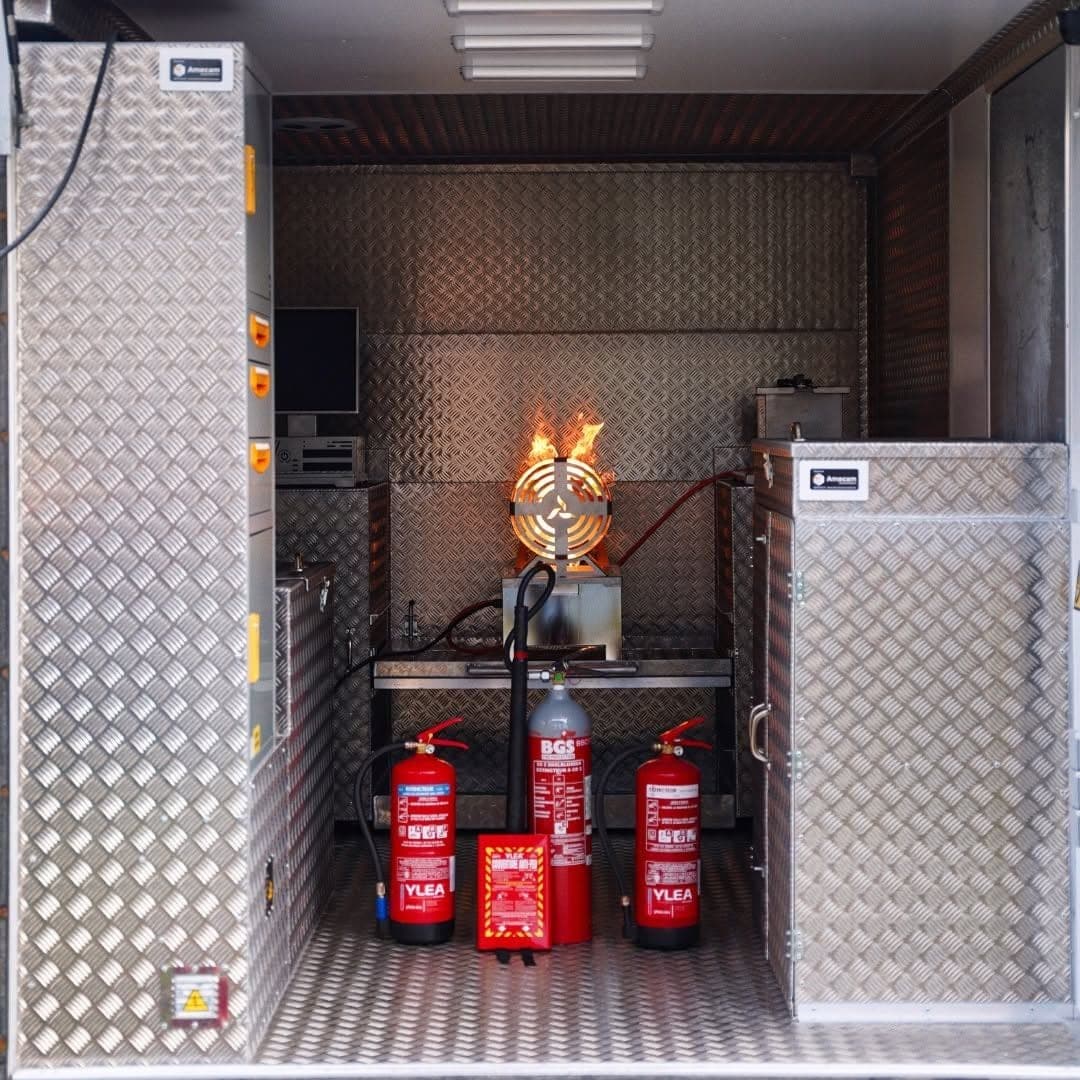 Cellule MD Safety en exercice, flammes sur le simulateur du fond, trois extincteurs et une couverture anti-feu posés au sol