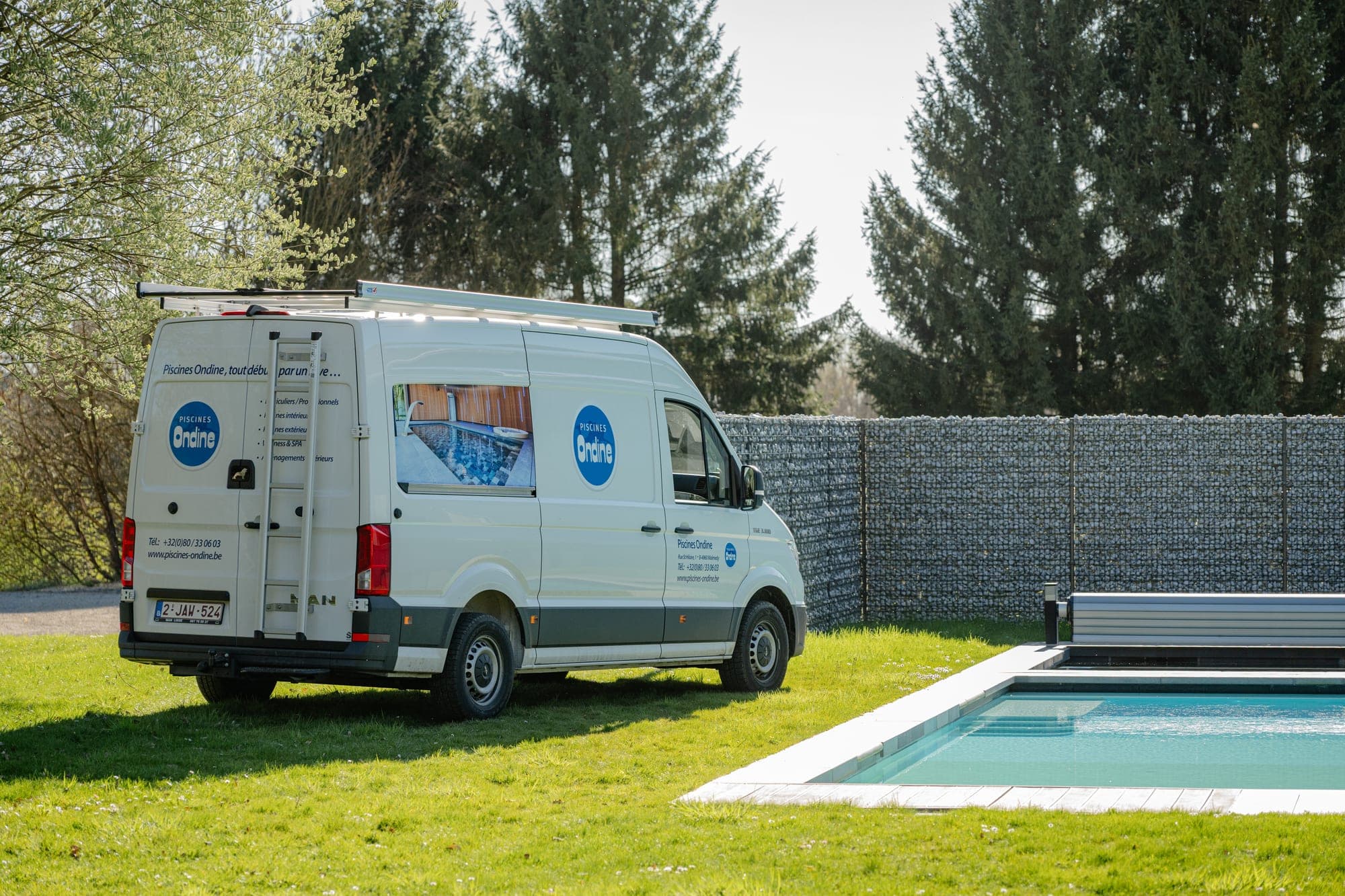 MAN TGE Piscines Ondine vu de trois quarts arrière, échelle d’accès au toit et panneau imprimé sur la vitre latérale