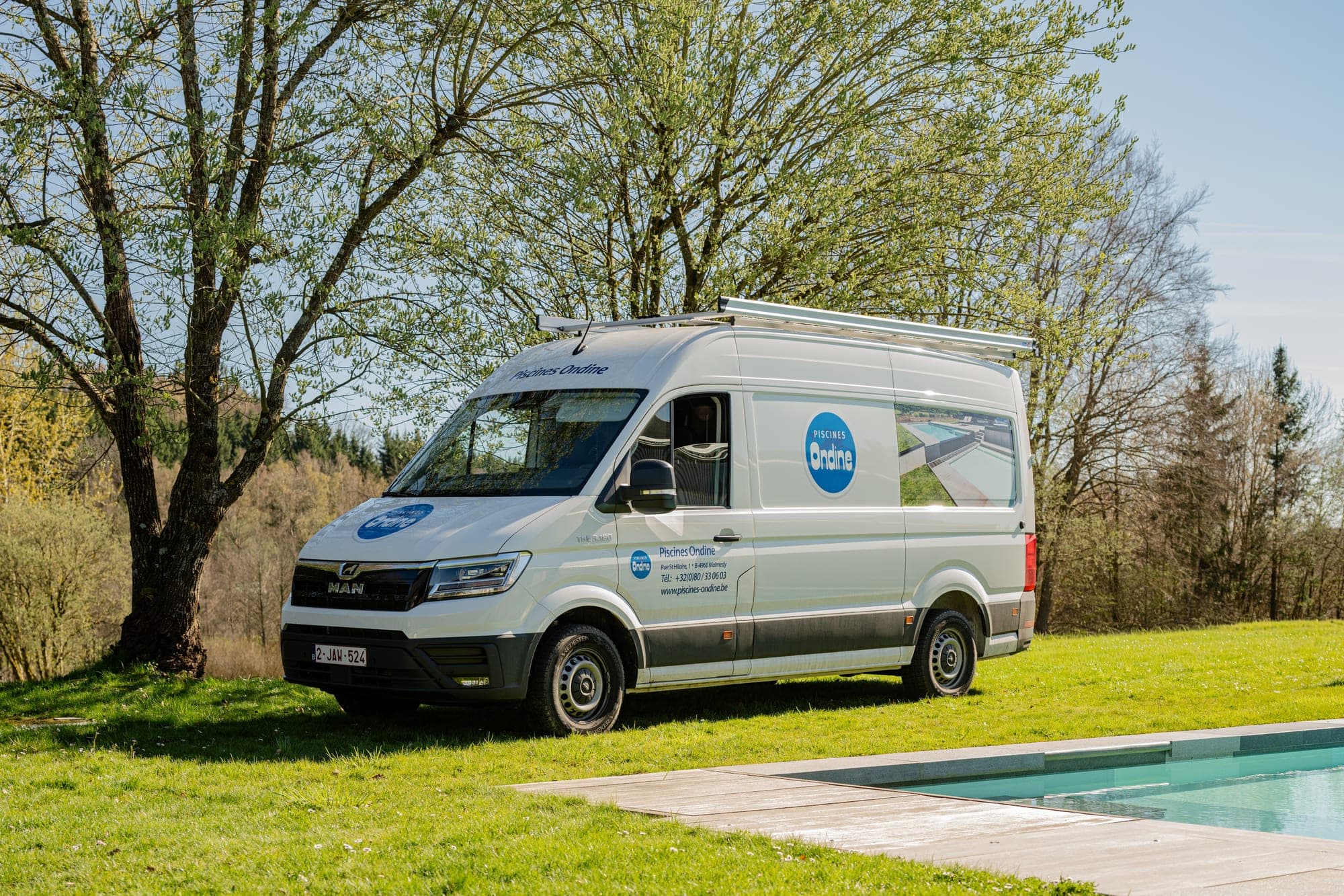 MAN TGE Piscines Ondine vu de trois quarts avant, galerie de toit et lettrage sur le pavillon, garé dans l’herbe au bord d’une piscine