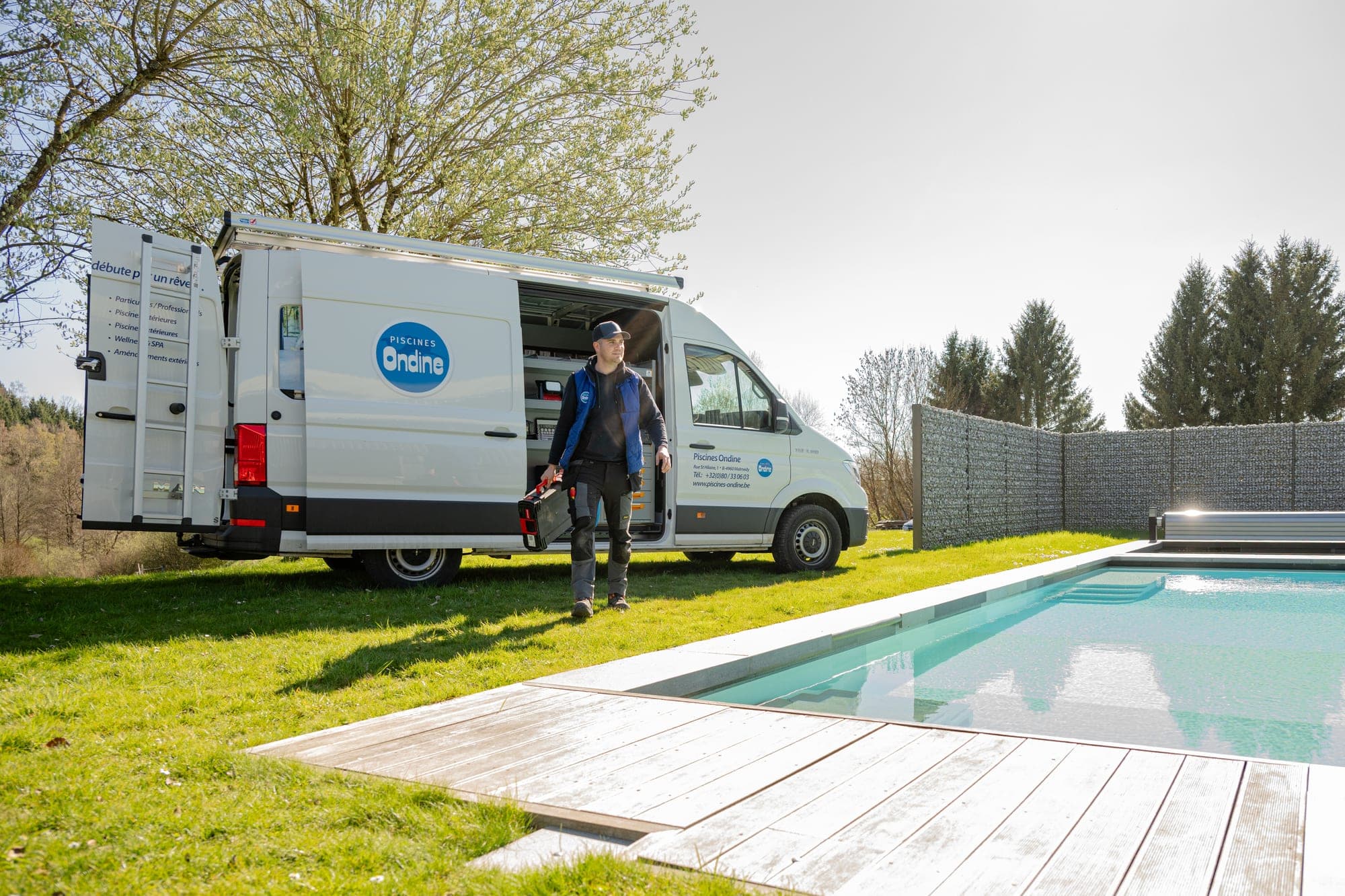 Technicien de Piscines Ondine sortant du fourgon avec une caisse à outils, porte latérale ouverte sur le rayonnage