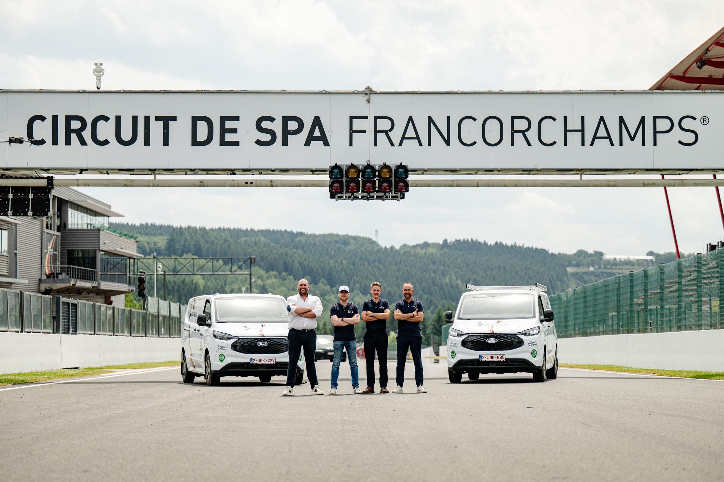 Quatre membres de l’équipe Amecam entre deux Ford Transit Custom aménagés, sur la ligne de départ du circuit de Spa-Francorchamps
